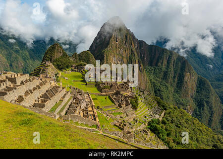 The lost Inca ruin city of Machu Picchu in the morning fog with its green terraced field and Huayna Picchu peak in the background near Cusco, Peru. Stock Photo