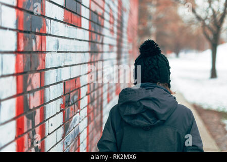Rear view of casual adult woman walking on city street in cold winter afternoon Stock Photo