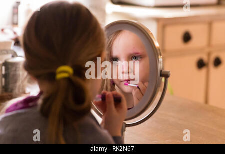 A 3 year old looking in the mirror and applying make up. Stock Photo