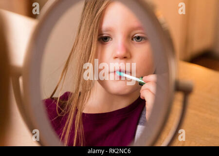 A 3 year old looking in the mirror and applying make up. Stock Photo