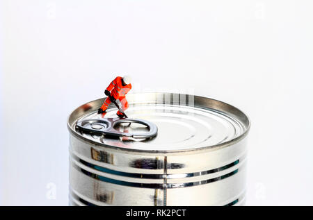 Conceptual diorama image of miniature figure workman trying to open a tin can, Stock Photo