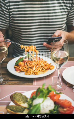 Italian dinner at bistrot with caprese salad with mozzarella, tomatoes, basil, pesto toasts, spaghetti pasta with shrimps, white wine. Man eating past Stock Photo
