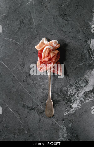 Antipasto meat assorti of sliced jamon, salami, chorizo sausage on fork over black marble background. Flat lay, space. Appetizer concept Stock Photo