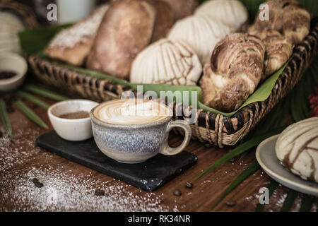 coffee and sugar on tile with a basket of pastries, on wood and with palm leaves Stock Photo