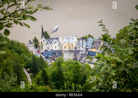 Boat sailing away in Hallstatt, an Austrian Alps mountain village, as seen from above, in a late summer day. The town church with close together house Stock Photo