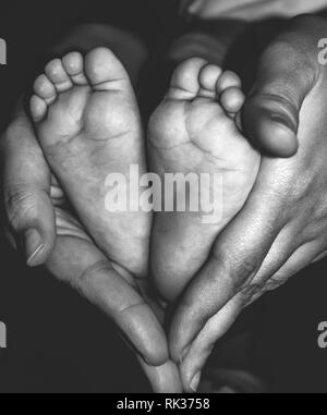 Baby feet in mother hands. Tiny Newborn Baby's feet on female Heart Shaped hands closeup. Beautiful Black and White conceptual image of Maternity. Stock Photo