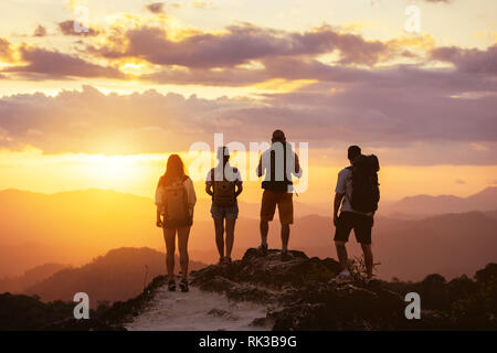 Group of four peope's silhouettes stands on mountain top and looks at sunset Stock Photo