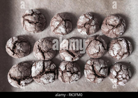 Freshly baked chocolate cookies with open cracks and sprinkled with white icing sugar lie on a still burning deck. Top view Stock Photo