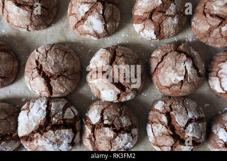 Freshly baked chocolate cookies with open cracks and sprinkled with white icing sugar lie on a still burning deck. Top view Stock Photo
