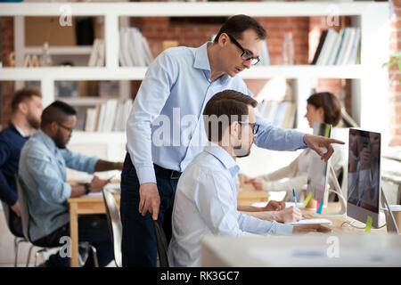 Executive manager helping male colleague with computer task in office Stock Photo