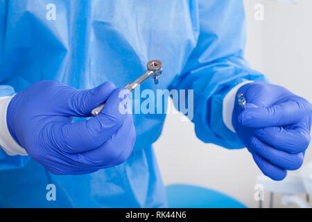 Close up picture of dental surgeon wearing blue gloves and coat, holding a dental drill Stock Photo