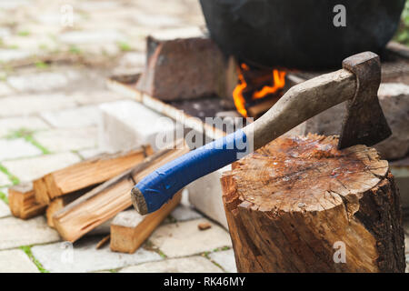Ax stuck in a log near cauldron standing on a bonfire Stock Photo