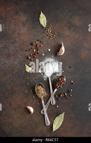 Food cooking background with spices and sea salt on dark rustic table, top view, copy space. Various peppers, garlic, bay leaf, cumin, coriander, salt Stock Photo