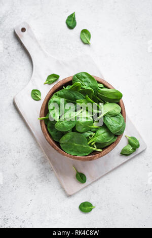 Baby spinach leaves in bowl on white background, top view, copy space. Clean eating, detox, diet food ingredient - green organic spinach. Stock Photo