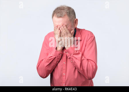 Senior man in red shirt covering his eyes with hands Stock Photo
