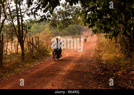 Cambodia, Koh Kong Province, Chi Phat, children returning from school along dusty road on motorcycles at end of day Stock Photo