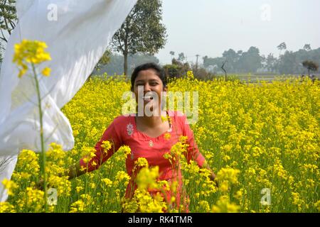 A young girl enjoy and flying her dhupatta in the air in a yellow rapeseed, mustard flowering field on a sunny day Stock Photo