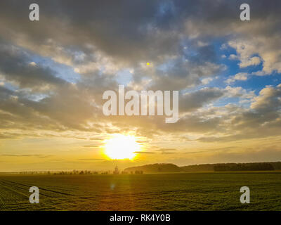 Panorama of a sunset on the cloudy sky over a green field, mountains in the back Stock Photo