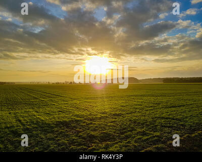Panorama of a sunset on the cloudy sky over a green field, mountains in the back Stock Photo
