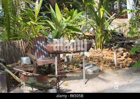 Rusted steel barbecue and a wheelbarrow in the garden (Ari Atoll, Maldives) Stock Photo