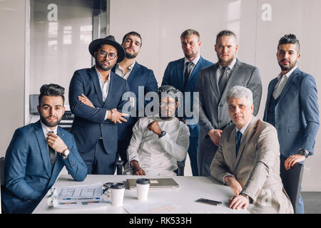 Group of multiethnic smart male professionals in formalwear with Middle eastern ethnicity investor sitting at mail in centre Stock Photo