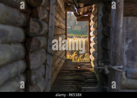 View to the small wooden house and lake shore through the narrow lane between two old log huts of ancient Lake Castle in Araisi Archaeological Museum  Stock Photo