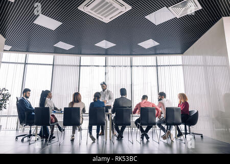 Rear view of business people sitting in a raw and listening a business coach at seminar at spacious modern conference room with panoramic windows Stock Photo