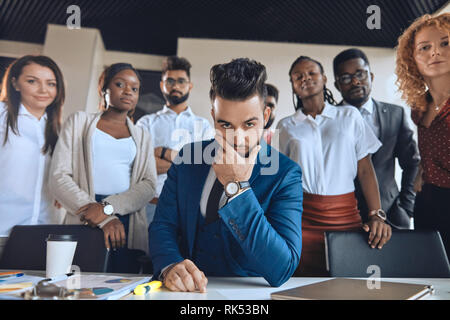 creative smart leader with advanced goals. handsome bearded boss touching his chin while his co-workers standing behind him Stock Photo