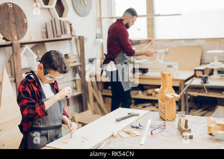 Family concept. Father and little son at wooden workshop standing at table using screwdriver in working process. Stock Photo
