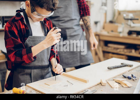 Family concept. Father and little son at wooden workshop standing at table using screwdriver in working process. Stock Photo