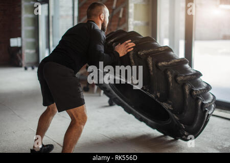 CrossFit Tire Technique. Powerful bodybuilder demonstrates rules and order of training with improvised powerlifting element in fitness club Stock Photo