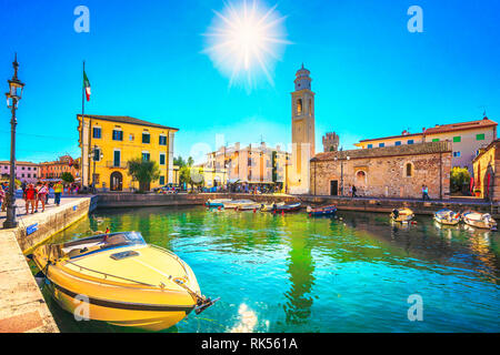 LAZISE, VENETO / ITALY - SEPTEMBER 28, 2018: Boats in old town port of Lazise and tourists walking in the morning. The town is a popular holiday desti Stock Photo