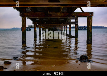 Landscape photograph taken under Lake Drive Pier from shoreline under cloudy sky on an inner harbour beach, Poole, Dorset. Stock Photo