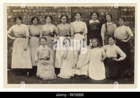 Early 1900's postcard group of cotton mill worker women and girls, tools held in belt, clogs, posing for a photograph in the mill grounds, Radcliffe, Lancashire, England, U.K. circa 1915
