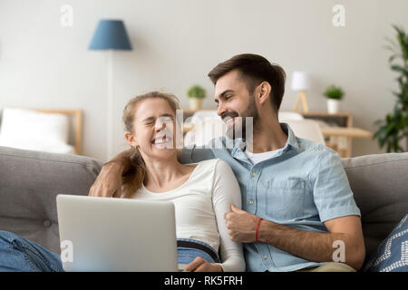 Happy young couple laughing relaxing on couch with laptop Stock Photo