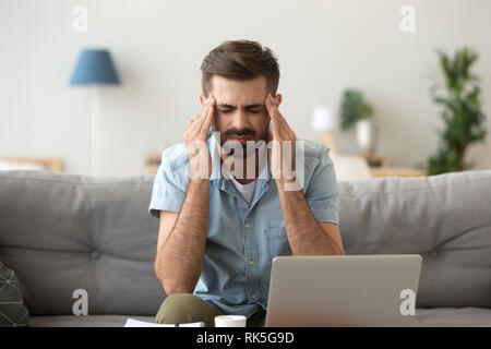 Tired stressed young man suffering from headache after computer work Stock Photo