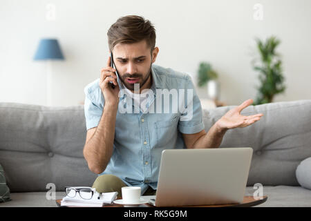Angry man talking on phone disputing over computer laptop problem Stock Photo