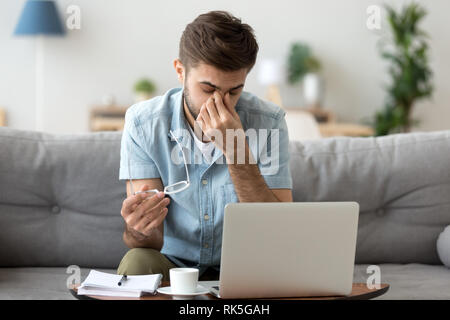 Tired young man feeling eye strain headache after computer work Stock Photo