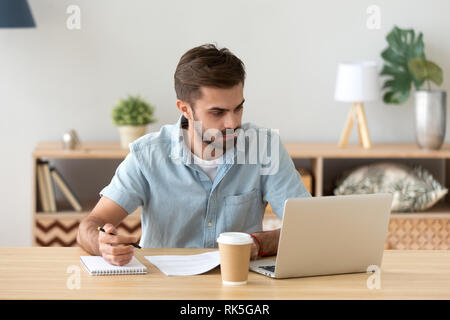 Serious man looking at laptop making notes working with documents Stock Photo