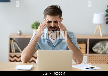 Stressed tired man having terrible headache after computer work Stock Photo