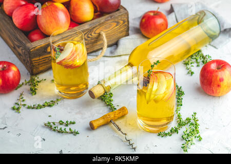 Hard apple cider cocktail with fall fresh thyme and star anise. Bottle and glasses of homemade organic apple cider with fresh apples in box, light con Stock Photo