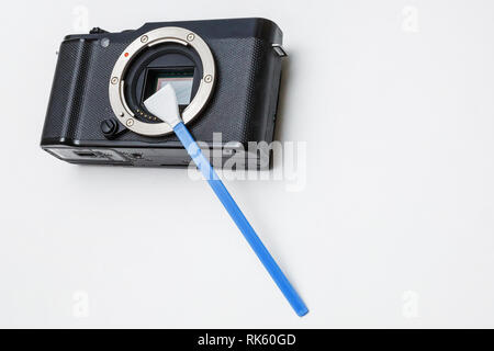 Close-up of mirrorless digital APS-C dirty camera matrix sensor cleaning and maintenance with swab, photographer cleaning photocamera on white backgro Stock Photo