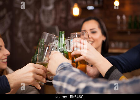 Happy young friends clinking beer bottles. Having fun in hipster pub. Stock Photo
