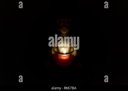 buddha holding a glass can with a candle in it. dark environment creepy and spiritual atmosphere. religion Stock Photo