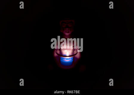 buddha holding a glass can with a candle in it. dark environment creepy and spiritual atmosphere. religion Stock Photo