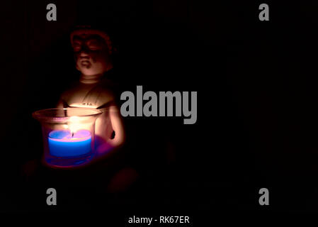 buddha holding a glass can with a candle in it. dark environment creepy and spiritual atmosphere. religion Stock Photo