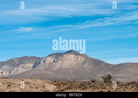 Ravine and rocky desert terrain on one side and sandy desert on the other side leading up to tall barren mountains under bright blue sky with white clouds. Stock Photo
