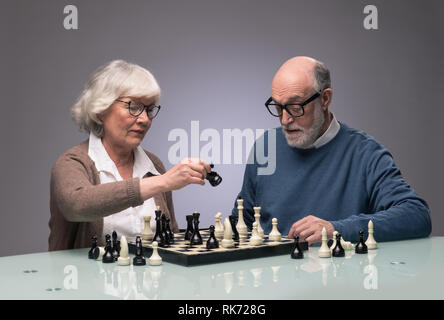 Elderly couple playing chess, studio shot on gray background Stock Photo