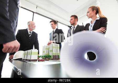 Business meeting of architects and investors looking at model of residential quarter houses and blueprints Stock Photo