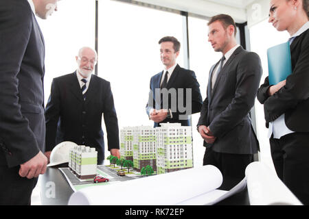 Business meeting of architects and investors looking at model of residential quarter houses and blueprints Stock Photo